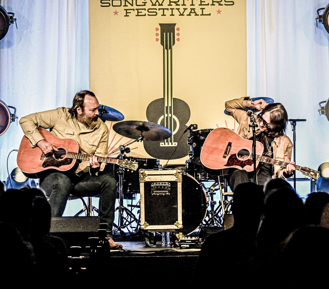 Songwriters playing in the round on the Opelika Songwriters Festival stage before a silhouetted audience
